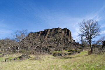 Low angle view of massive basalt rocky protrusion along a sloped meadow, with the horizon broken up...