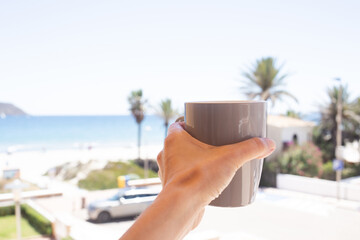 Enjoying a relaxing moment with a cup in hand by the beachside in a sunny coastal location