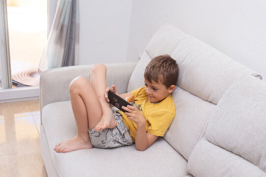 Child plays with mobile phone while slouching on the sofa, showing poor posture habits