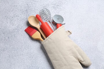 Different kitchen utensils in oven mitten on light table, above view