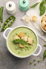 Tasty pea cream soup with croutons and basil served on grey table, flat lay