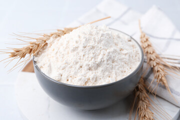 Wheat flour and spikes on white table, closeup