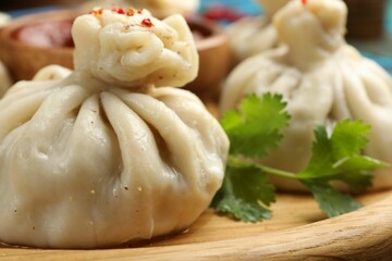 Delicious khinkali served with sauce on wooden plate, closeup