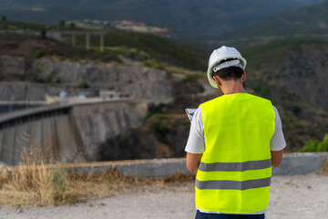 Engineer supervising water resources and renewable energy at dam, seen from behind while pointing...