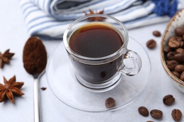 Cup of aromatic coffee, beans and star anise on white table, closeup