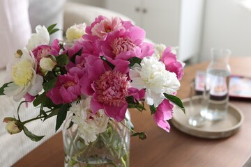 Bouquet of beautiful peonies and water on coffee table indoors, closeup. Interior design