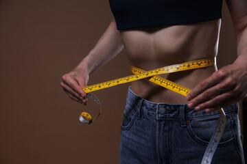 Anorexic woman measuring her waist on brown background, closeup
