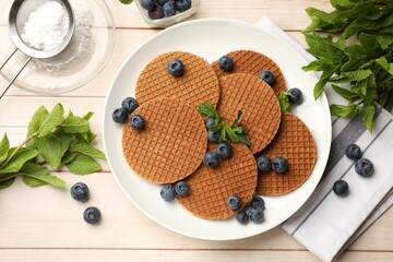 Tasty Dutch waffles (stroopwafels), mint and blueberries on light wooden table, flat lay
