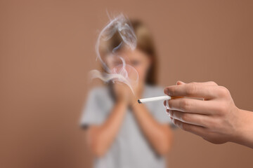 Passive smoking. Little girl covering her nose with hands because of man smoking nearby on pale brown background. Selective focus