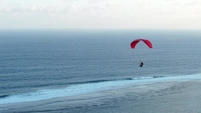 4K drone shot of a red paraglider gliding over the deep blue ocean, turning right and disappearing toward the horizon. Perfect for travel ads, freedom-themed content, and scenic visuals.
