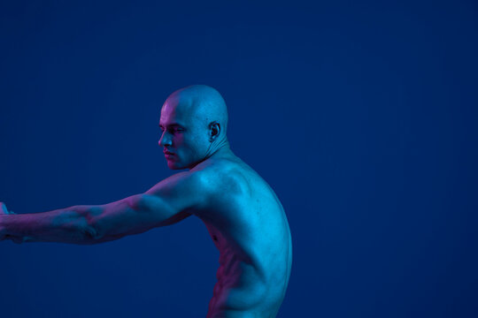 Fototapeta Bald man posing gracefully with outstretched arms, showcasing artistic expression in a captivating blue light. This image highlights the beauty of human form and emotion.    