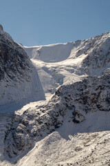 Majestic snow-covered mountain range with a glacier flowing down the rocky terrain under a clear...