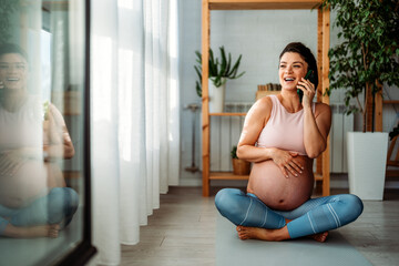 Pregnant sports woman taking a break from exercises and having phone call while relaxing at home