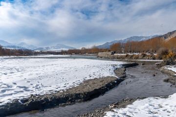 Winter River Scene with Snowy Banks and Himalayan Mountains in Ladakh
