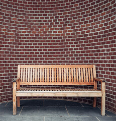 A wooden bench is sitting in front of a brick wall