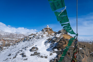 Snow-Covered Hilltop Stupa with Buddhist Prayer Flags in Ladakh, India