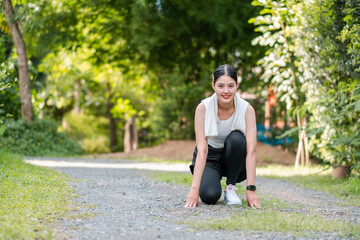 Woman in athletic wear kneeling on a gravel path, ready to run, with vibrant green trees and grass...