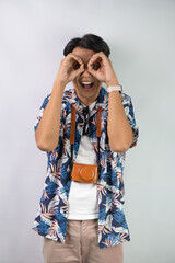 Happy young asian man wearing blue summer shirt is making peering through binoculars hand gesture,...