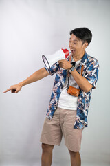 Handsome young asian man wearing blue summer shirt is shouting using a megaphone, isolated over white background.