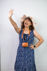 Happy beautiful young asian woman wearing blue summer dress and beach straw hat is shielding her...