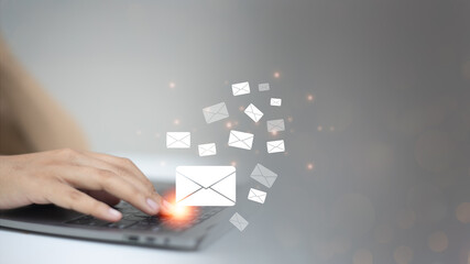 Close-up of a hand sending emails from a laptop keyboard with flying envelope icons and a warm glow.