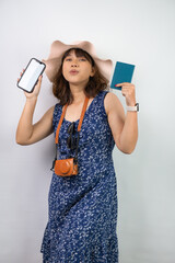 Naklejka premium Beautiful young asian woman wearing blue summer dress and beach straw hat is holding smartphone with blank screen and indonesian passport, isolated over white background.