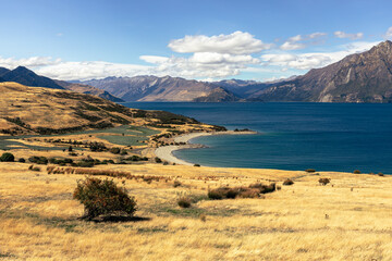 A wide panoramic view of Lake Wanaka's deep blue waters and distant mountain ranges under a partly...