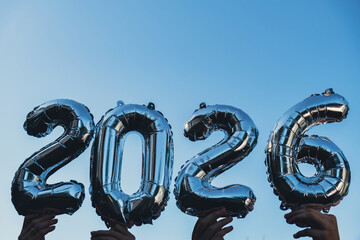 Happy new year 2026 metallic balloons on blue sky background. Greeting card silver foil balloons...