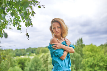Obraz premium A woman in a blue dress is standing in a grassy field. She is looking at the camera with a serious expression. The scene has a peaceful and serene atmosphere, with the lush green grass