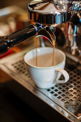 Close up of fresh espresso flows from coffee machine into a white cup