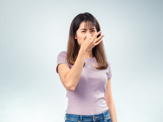 Asian woman in a purple shirt holds her nose in disgust, reacting to a bad smell with a frown and...
