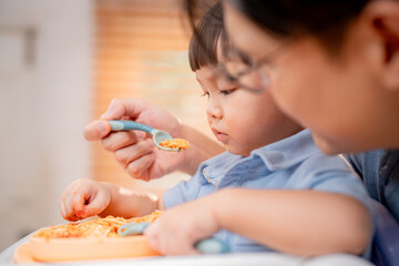 Family meal time with young child enjoying food and parent assisting in a bright, cozy kitchen...