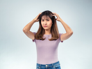 Asian woman in a purple t-shirt and jeans scratching her head with a confused and puzzled expression, standing against a light background
