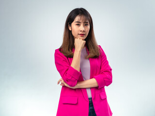 Asian woman in pink blazer and purple t-shirt standing with hand on chin, looking up with serious...