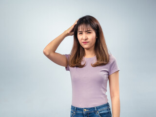 Asian woman in a purple t-shirt and jeans scratching her head with a confused and puzzled expression, standing against a light background