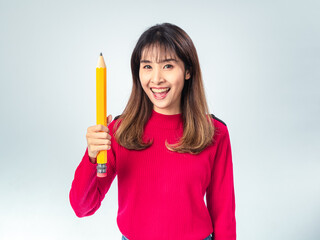 Asian woman in red sweater holding a giant yellow pencil and smiling with enthusiasm, posing against a light grey background, expressing creativity and cheerful energy