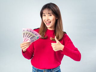 Asian woman in red sweater smiling while holding a fan of Indonesian 100,000 Rupiah banknotes in...