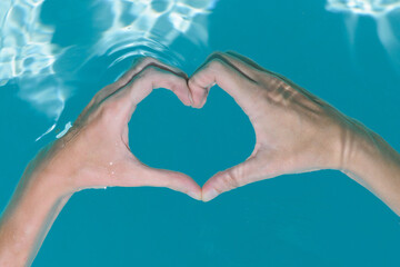 Hands creating a heart shape underwater in water of swimming pool. 