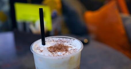 Female barista stirring frothy cappuccino, chocolate dust topping, relaxing near sunlit cafe window
