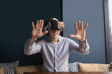 Cheerful man using virtual reality headset while sitting against wall