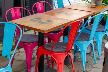 Colorful metal chairs and a wooden table with numbers in a restaurant outdoor seating area, set on a paved surface