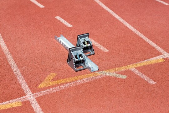metal starting block is resting on red track, flat vector design showing white lanes, yellow arrow