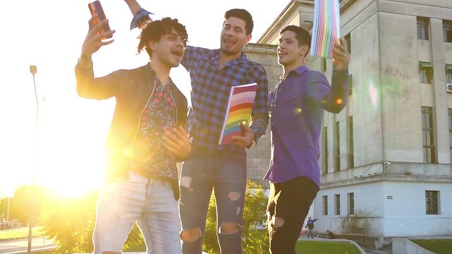 Three Latin gays students holding rainbow notebooks and recording a self-tape with smartphone outside university.