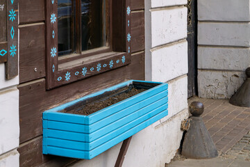 Blue wooden flower box mounted under a window decorated with a folk floral pattern on a...