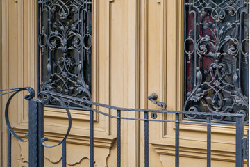 Decorative wooden door with ornate wrought iron grilles and stained glass behind them. In the...