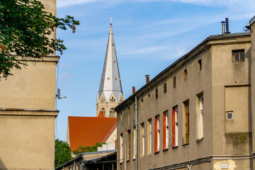 View of a church tower in Łódź rising between old, neglected buildings. The tall spire with a...