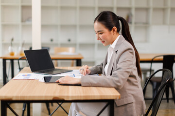Asian professional analyst business woman sitting at office desk working on laptop thinking on project plan, analyzing marketing or financial data online, watching elearning webinar.