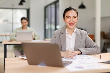 Obraz premium Asian professional analyst business woman sitting at office desk working on laptop thinking on project plan, analyzing marketing or financial data online, watching elearning webinar. 