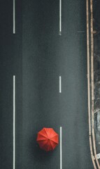 Overhead view of a solitary red umbrella on a dark asphalt road with lane markings