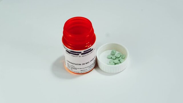 An open container of Lovastatin with pills poured into cap rotating right to left.